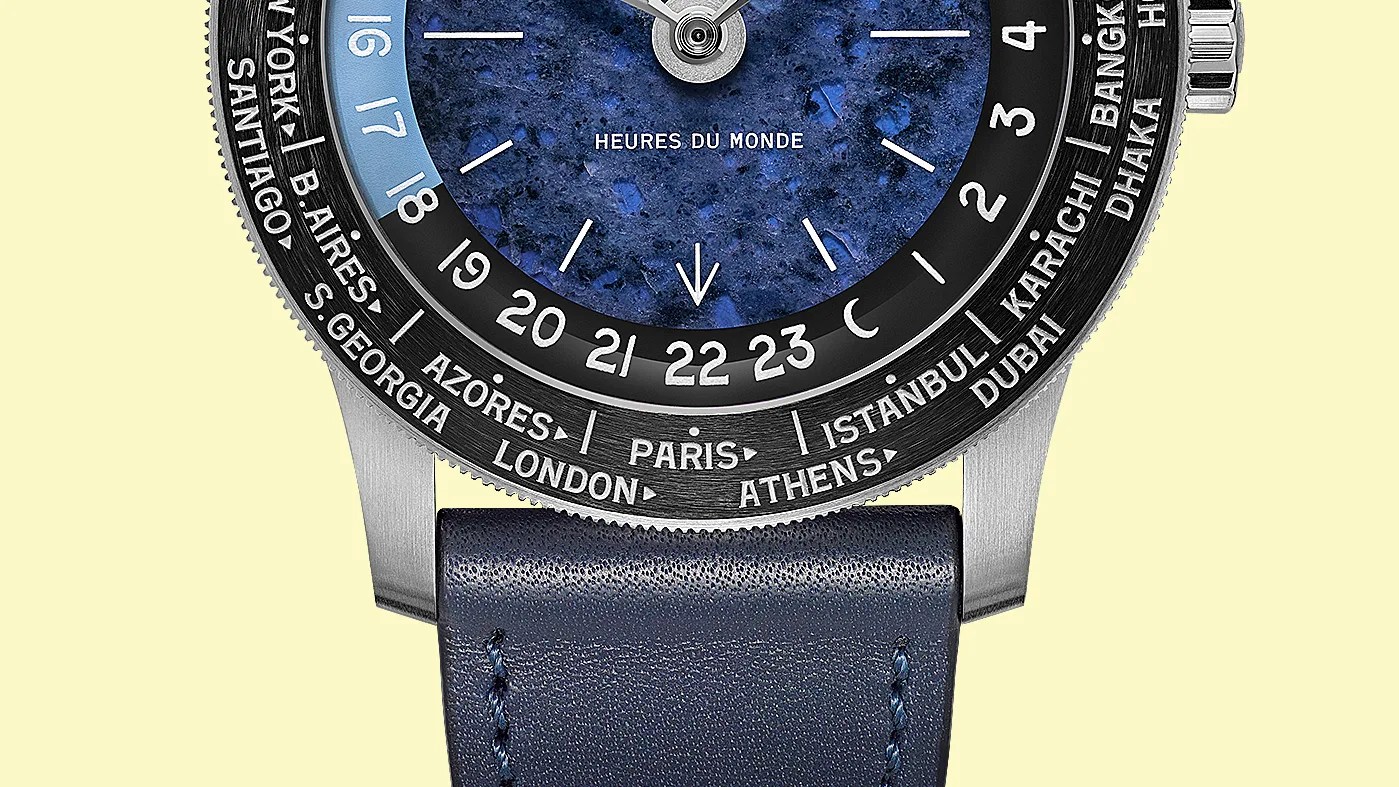 Close-up of a watch face with a blue textured dial, world city names on the bezel, and a blue leather strap.