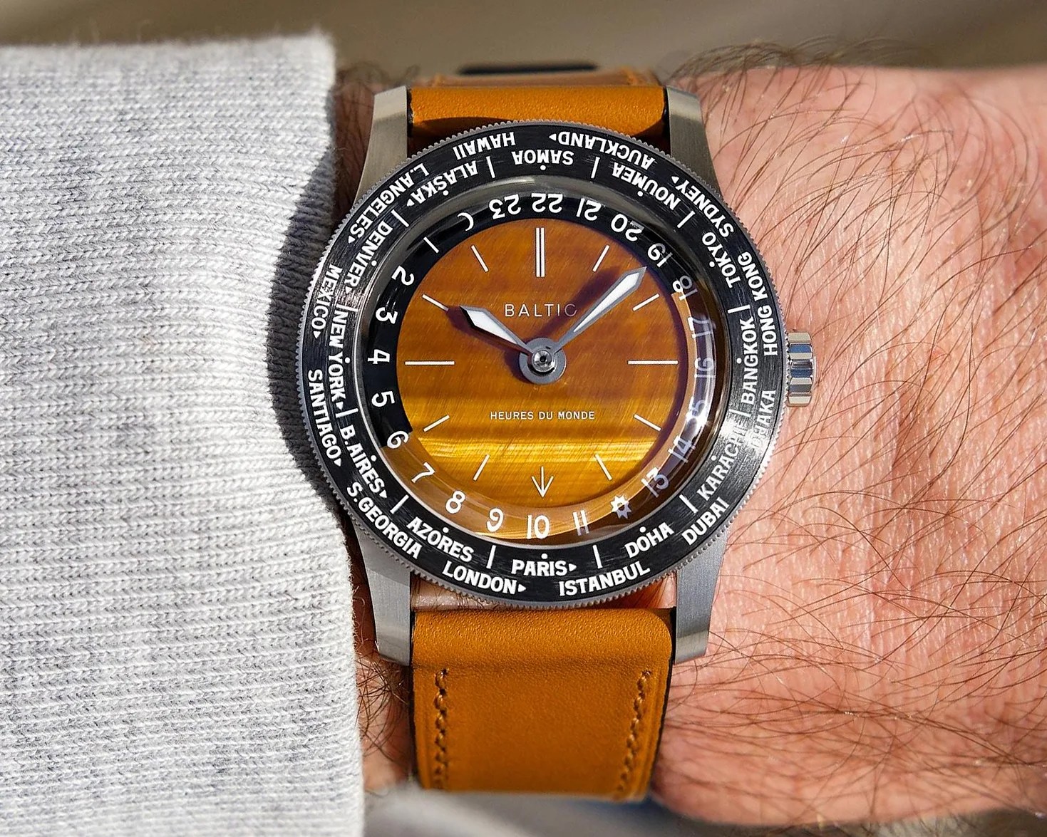 Wristwatch with a brown leather strap, orange sunburst dial, and black bezel showing world city names.