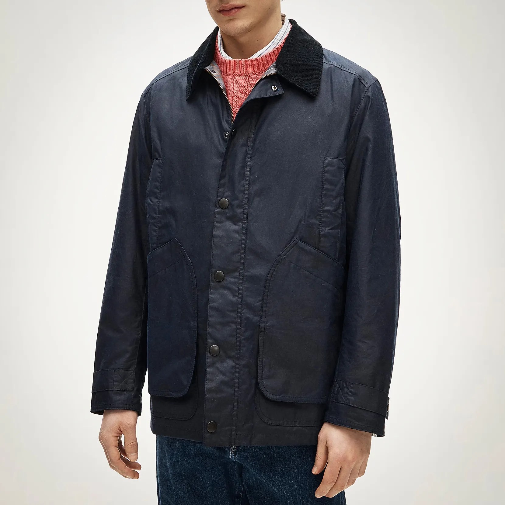 Navy blue waxed cotton jacket with black corduroy collar and snap button closure worn over a pink sweater.