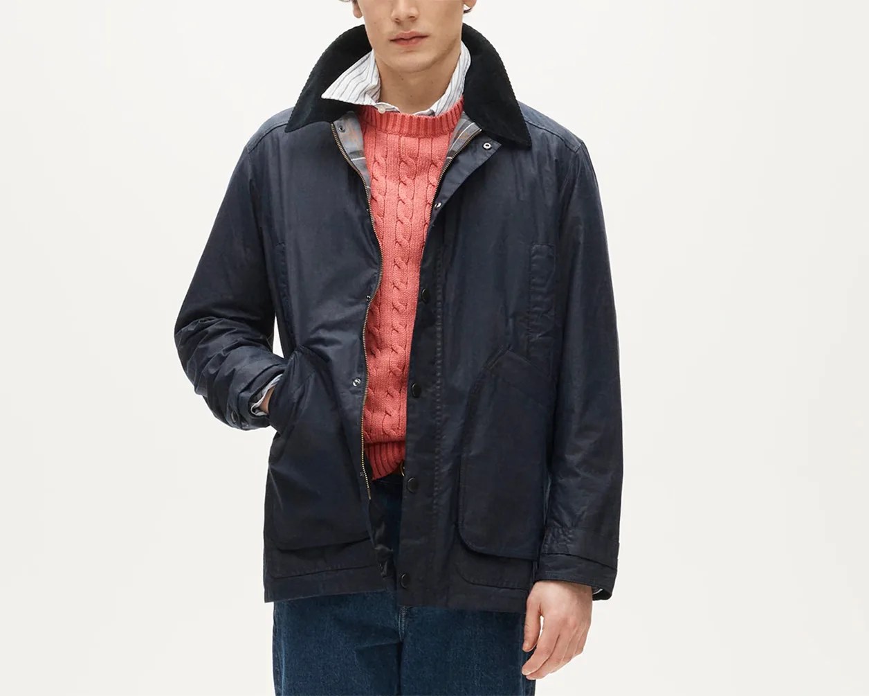 Navy waxed cotton jacket with black corduroy collar worn over a coral cable-knit sweater and striped shirt.