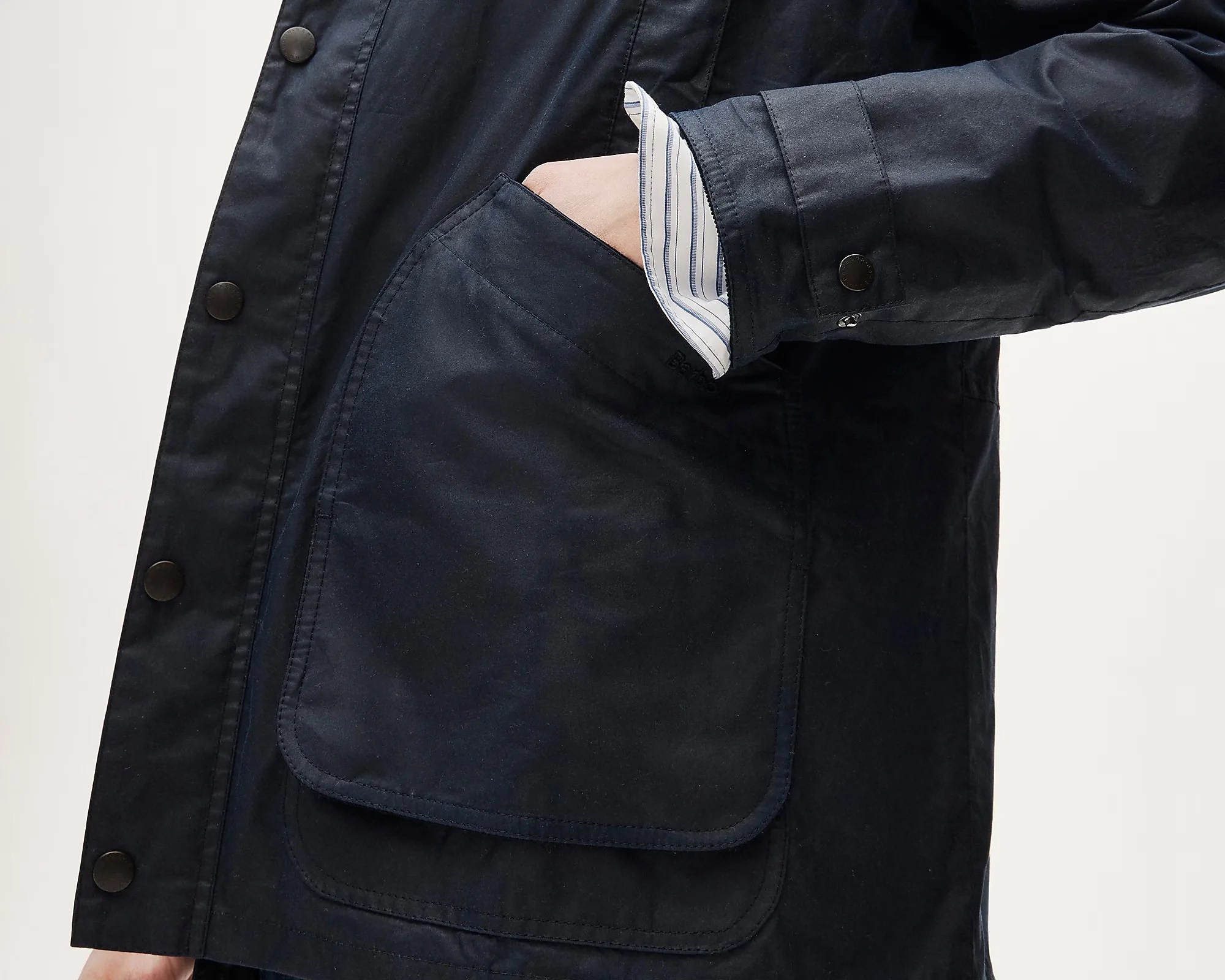 Close-up of a navy blue jacket pocket with a hand inside and a striped shirt cuff visible.