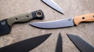 Five knives with various blade shapes and handle materials, including wood and textured synthetic, arranged on a stone surface.