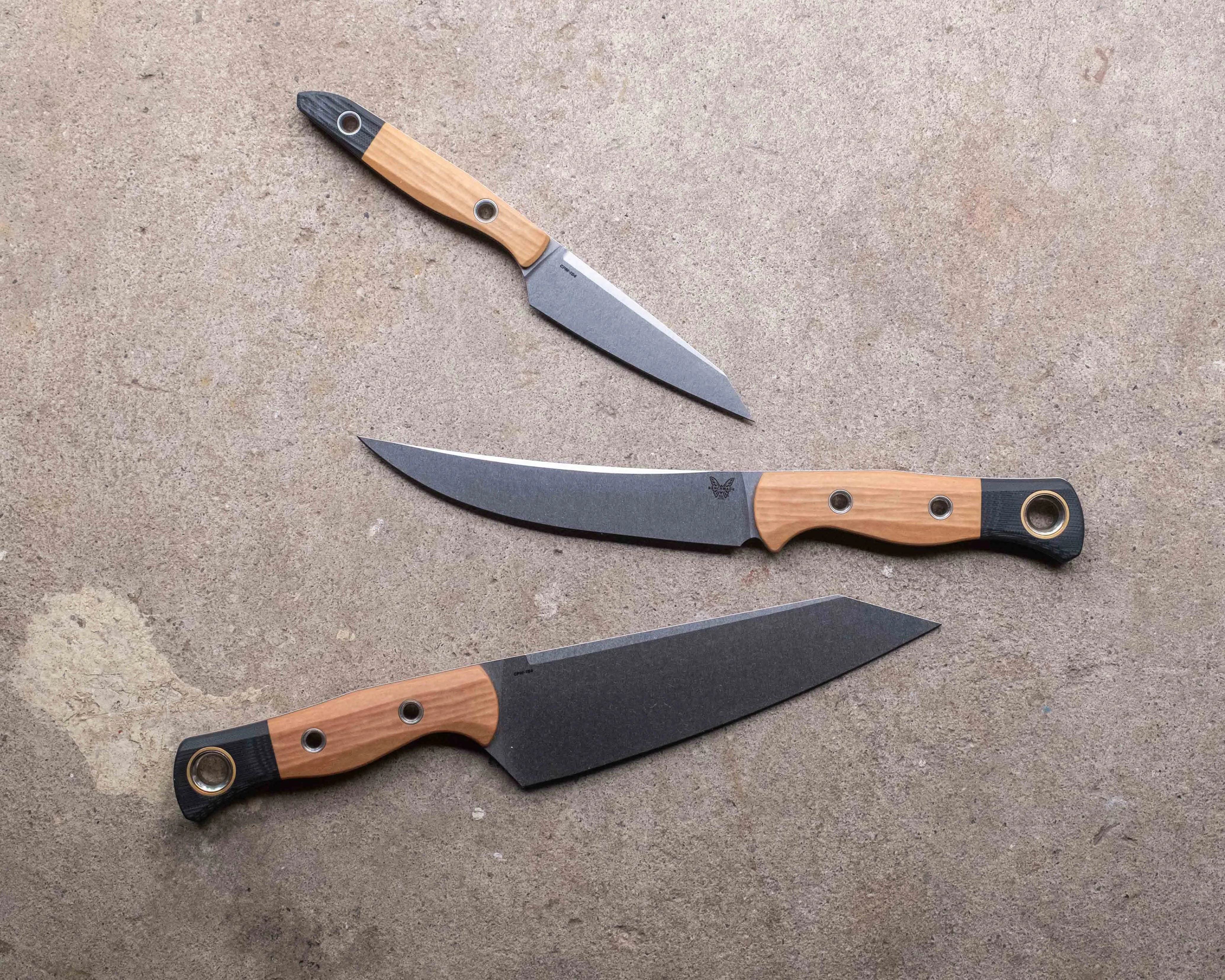 Three kitchen knives with wooden handles and black blades laid out on a concrete surface.