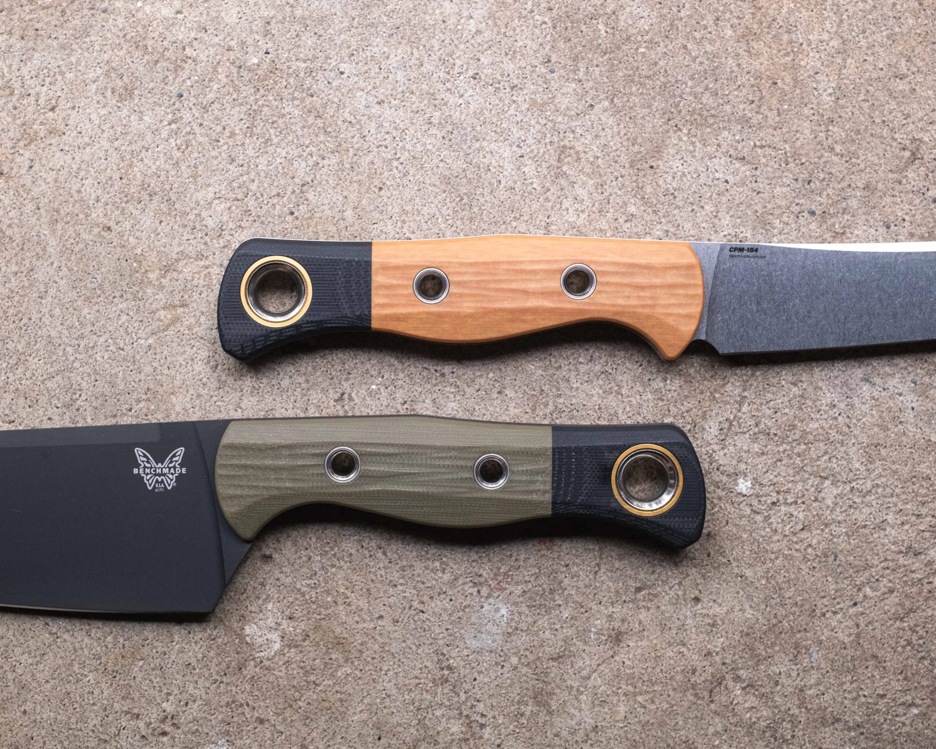 Two Benchmade knives with textured handles, one with a wood finish and the other with an olive green finish, on a stone surface.