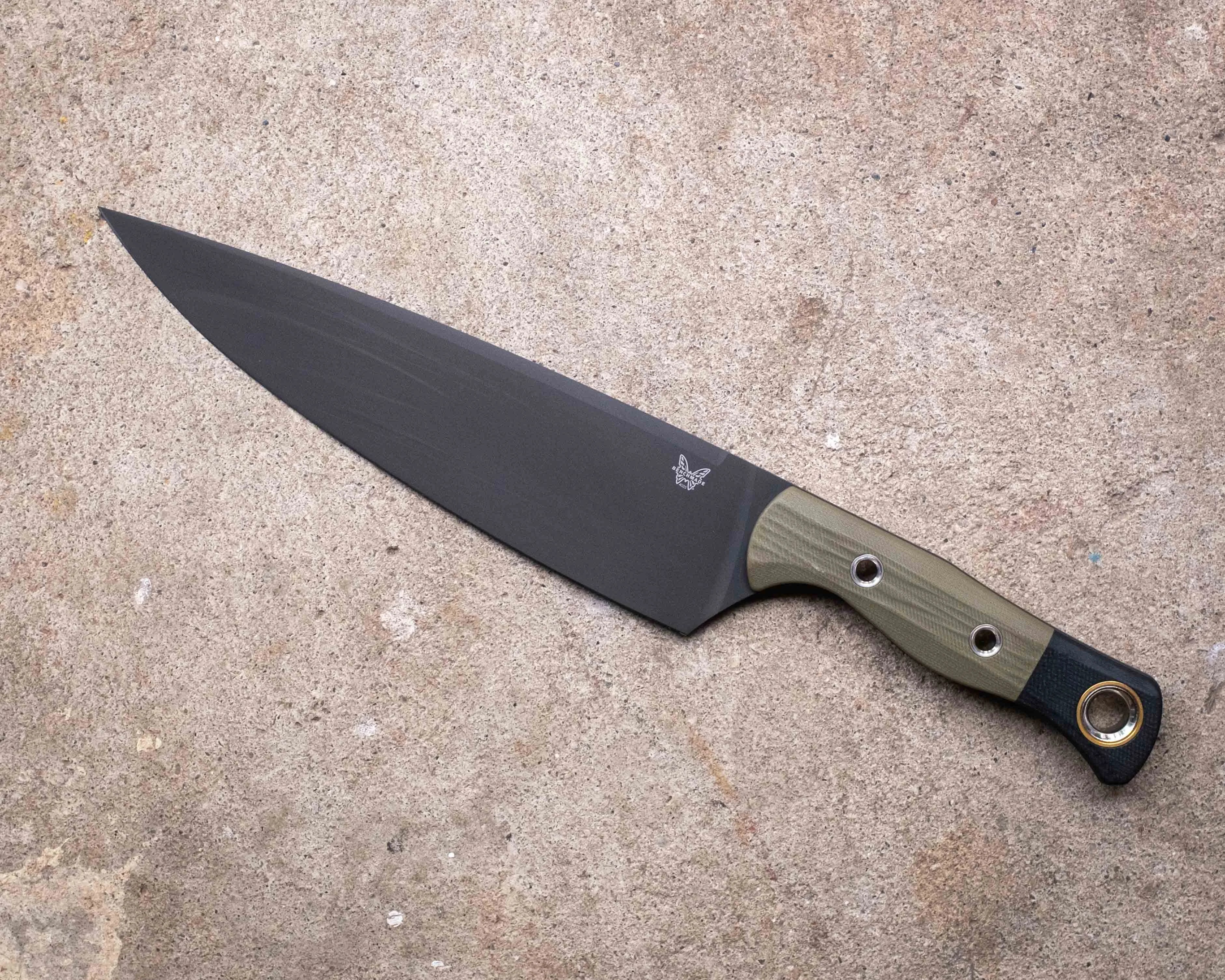 Chef knife with a black blade and green and black handle on a textured stone surface.