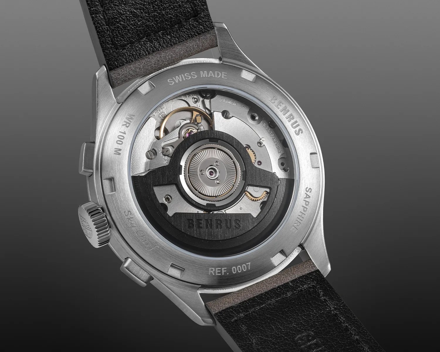 Back of a Benrus wristwatch showing the automatic movement through a sapphire case back with black leather strap.