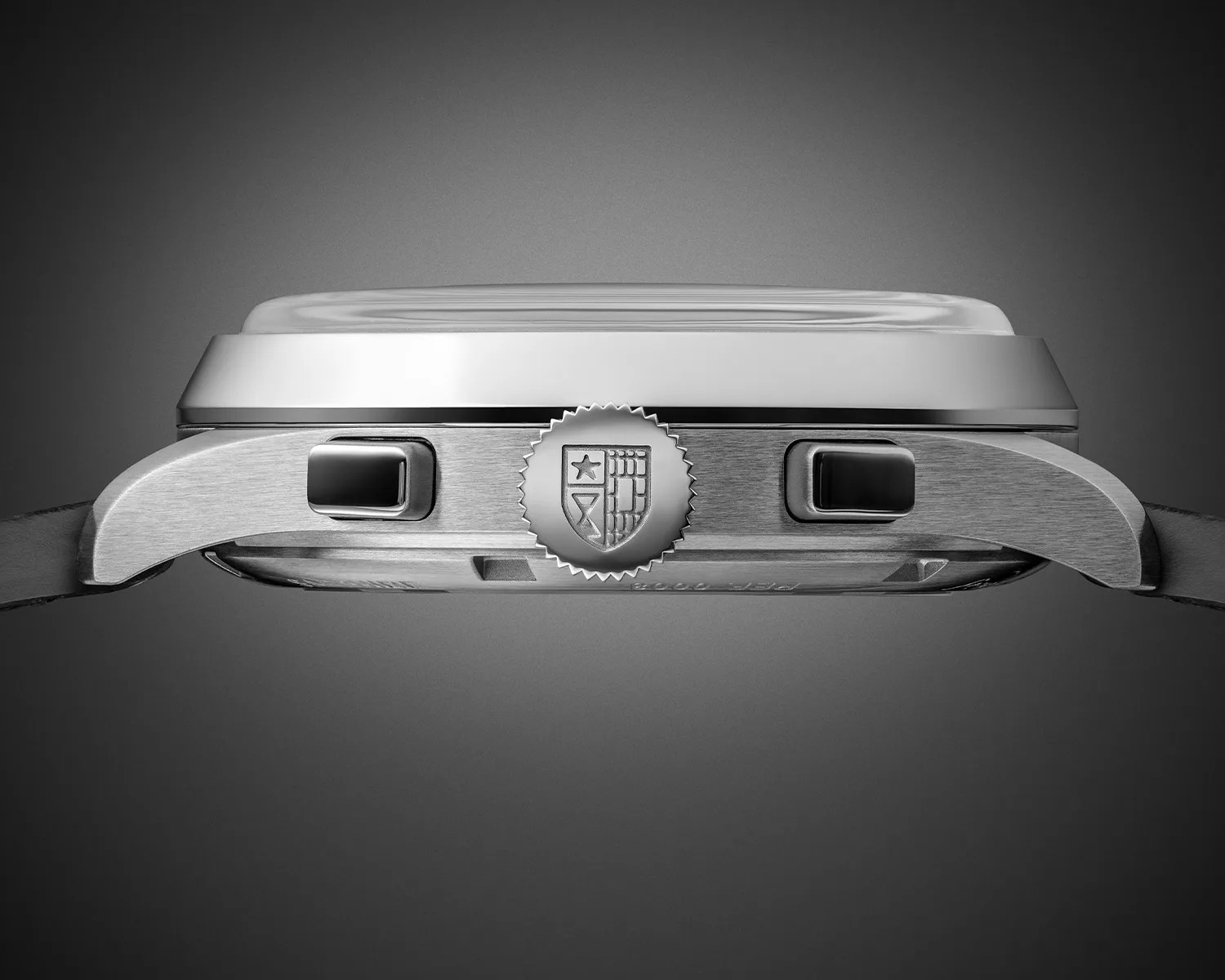 Side view of a stainless steel wristwatch case with two rectangular pushers and a crown featuring an embossed shield emblem.