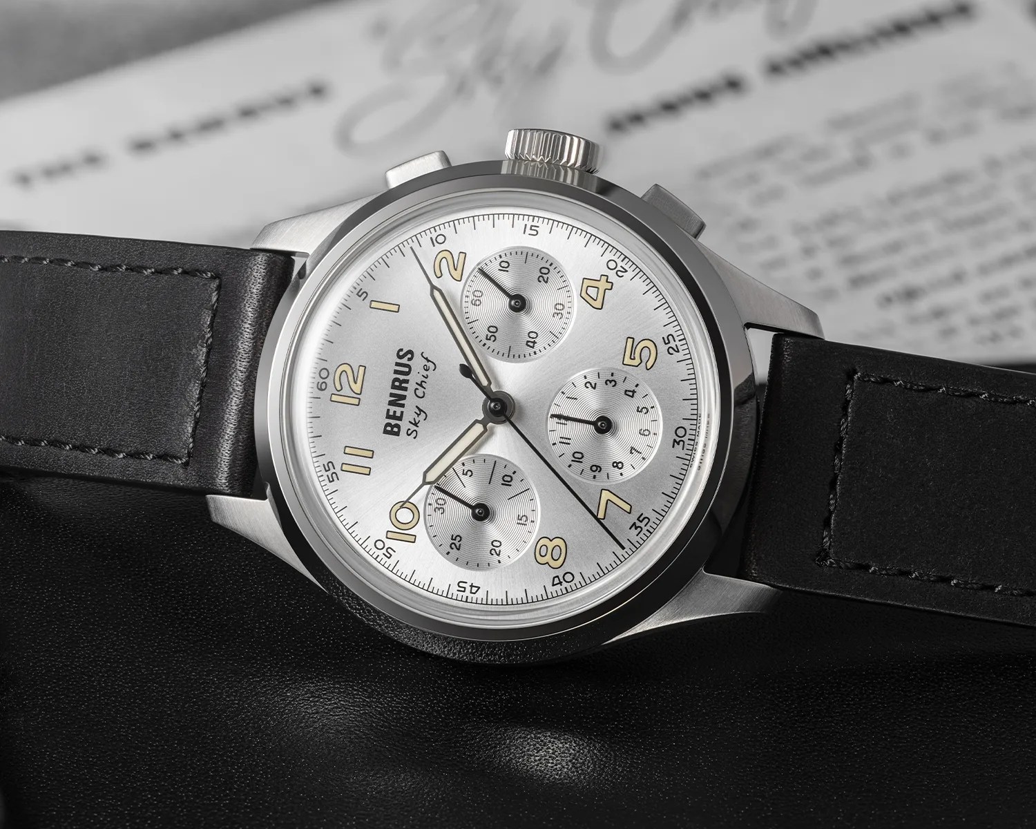 Silver Benrus Sky Chief chronograph watch with black leather strap on a black surface.