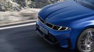 Front view of a blue BMW car with illuminated headlights and spinning front wheel on a road.