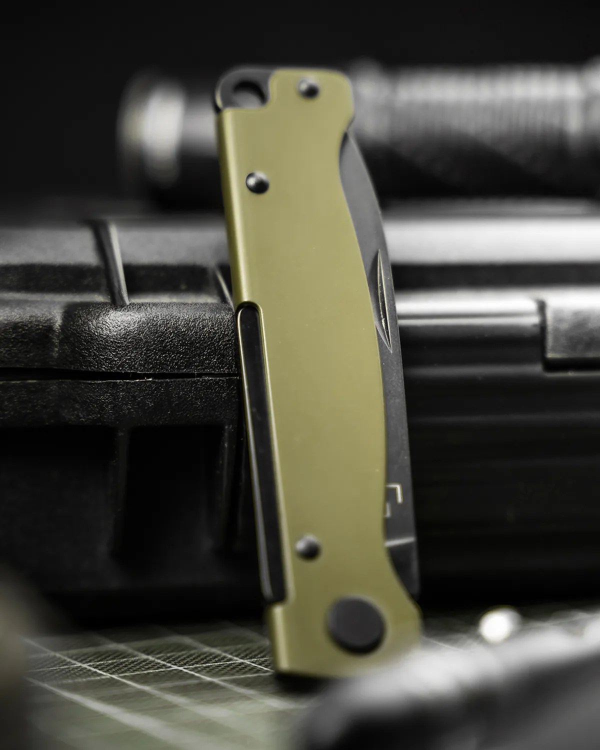 Folded olive green and black pocket knife resting vertically on a black textured case.