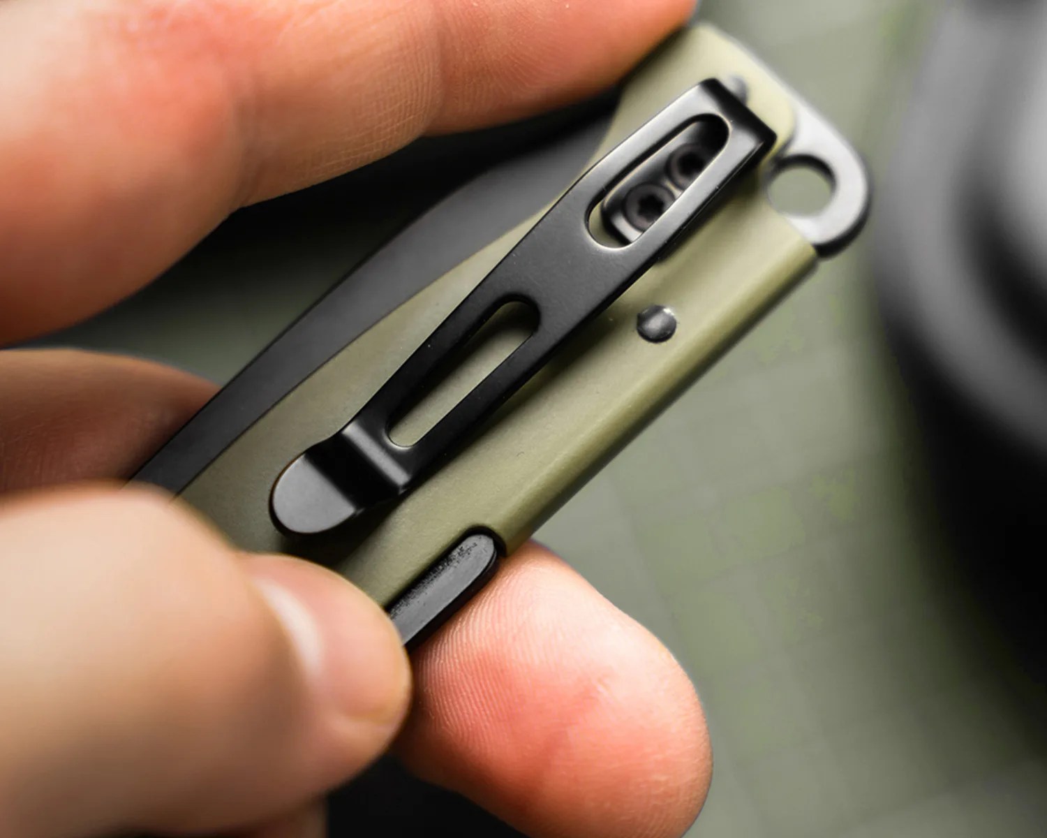 Close-up of a hand holding a green folding knife with a black metal pocket clip.