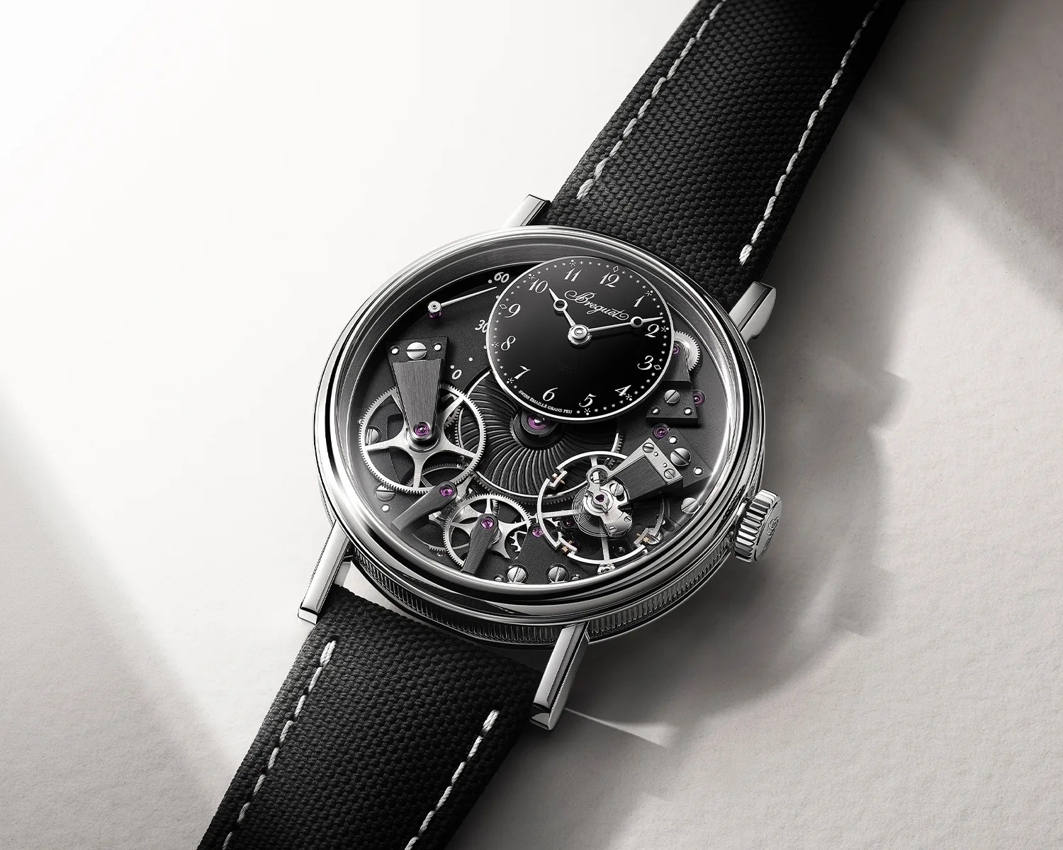 Silver mechanical wristwatch with visible gears and a small black dial on a black fabric strap.