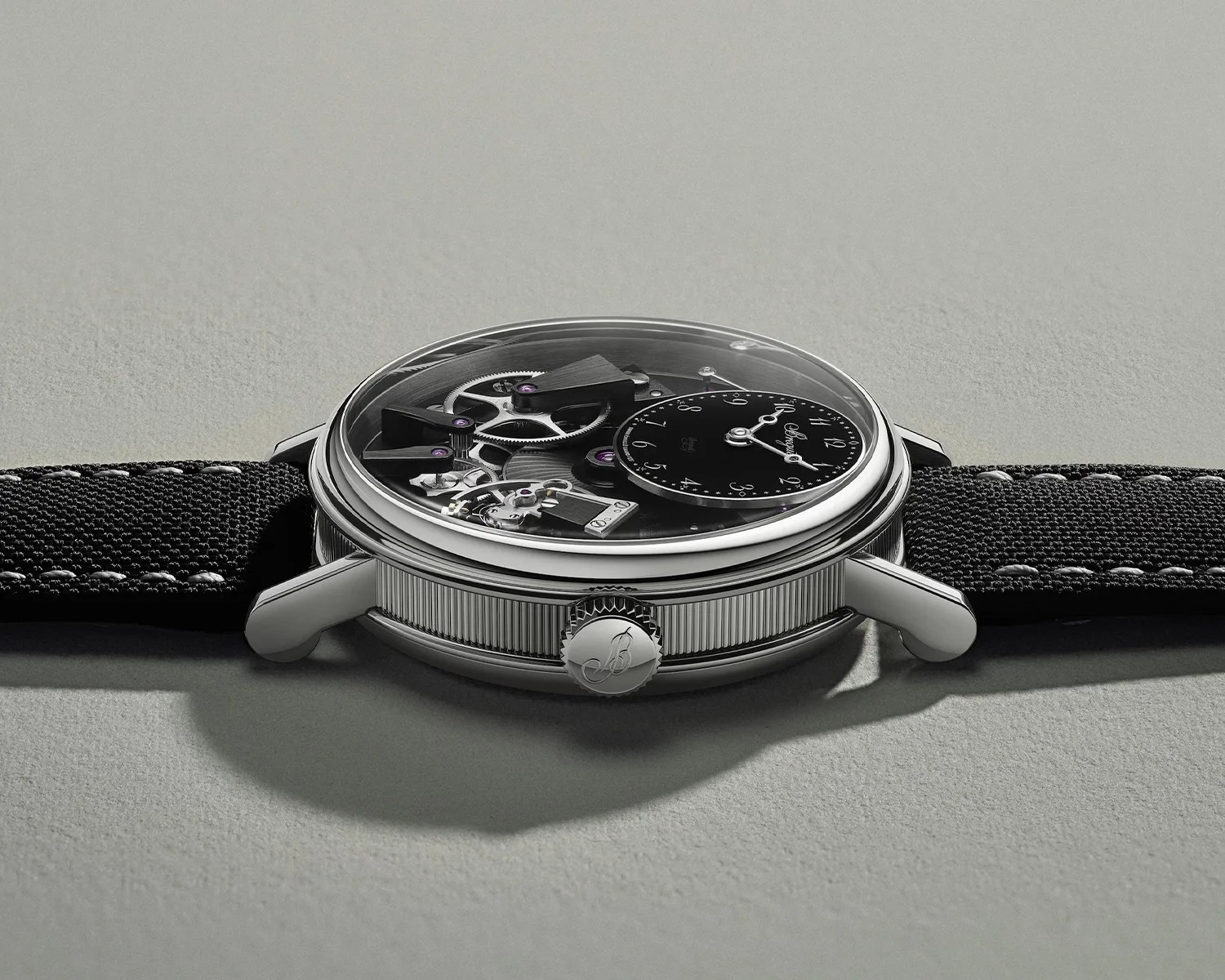 Side view of a mechanical wristwatch with a black textured strap and a silver case showing visible gears and a small black dial.