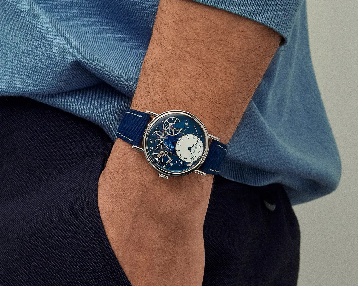 Silver wristwatch with blue mechanical dial and white subdial on a blue fabric strap worn on a wrist.