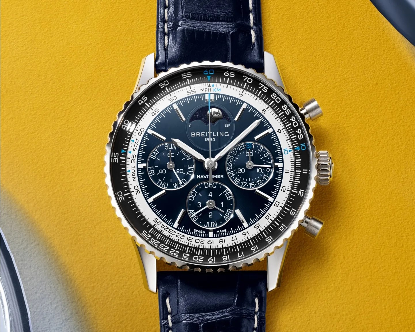 Breitling Navitimer wristwatch with black dial, multiple subdials, silver case, and black leather strap on yellow surface.
