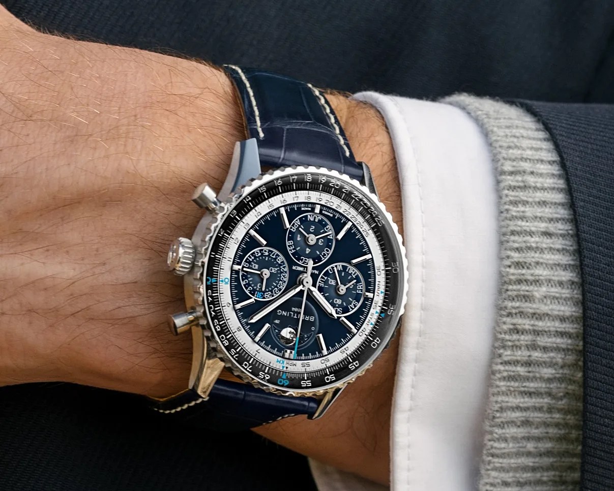 Silver Breitling chronograph watch with blue dial and leather strap worn on a wrist.