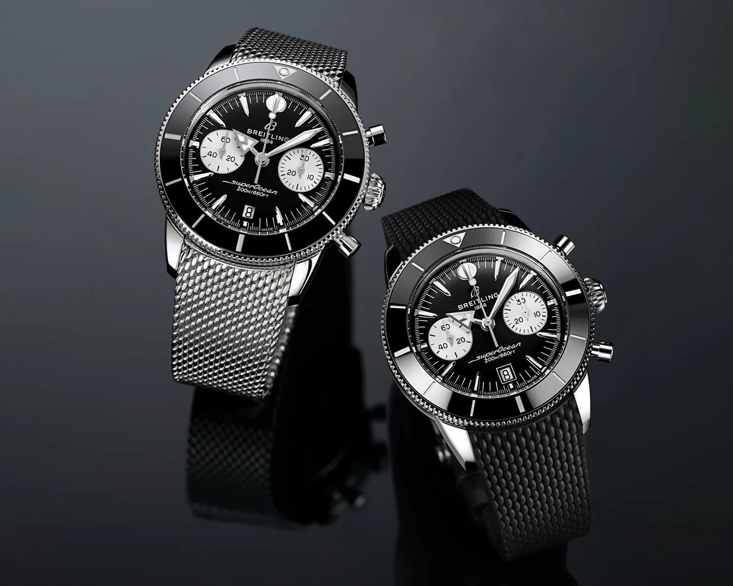 Two Breitling Superocean watches with black dials and white subdials, one with a silver mesh strap and the other with a black textured strap.