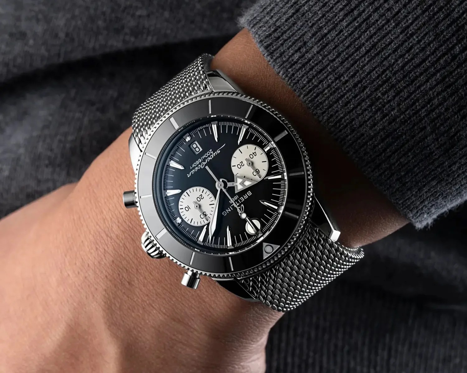 Breitling Superocean wristwatch with black dial, two white subdials, and silver mesh strap on a wrist.