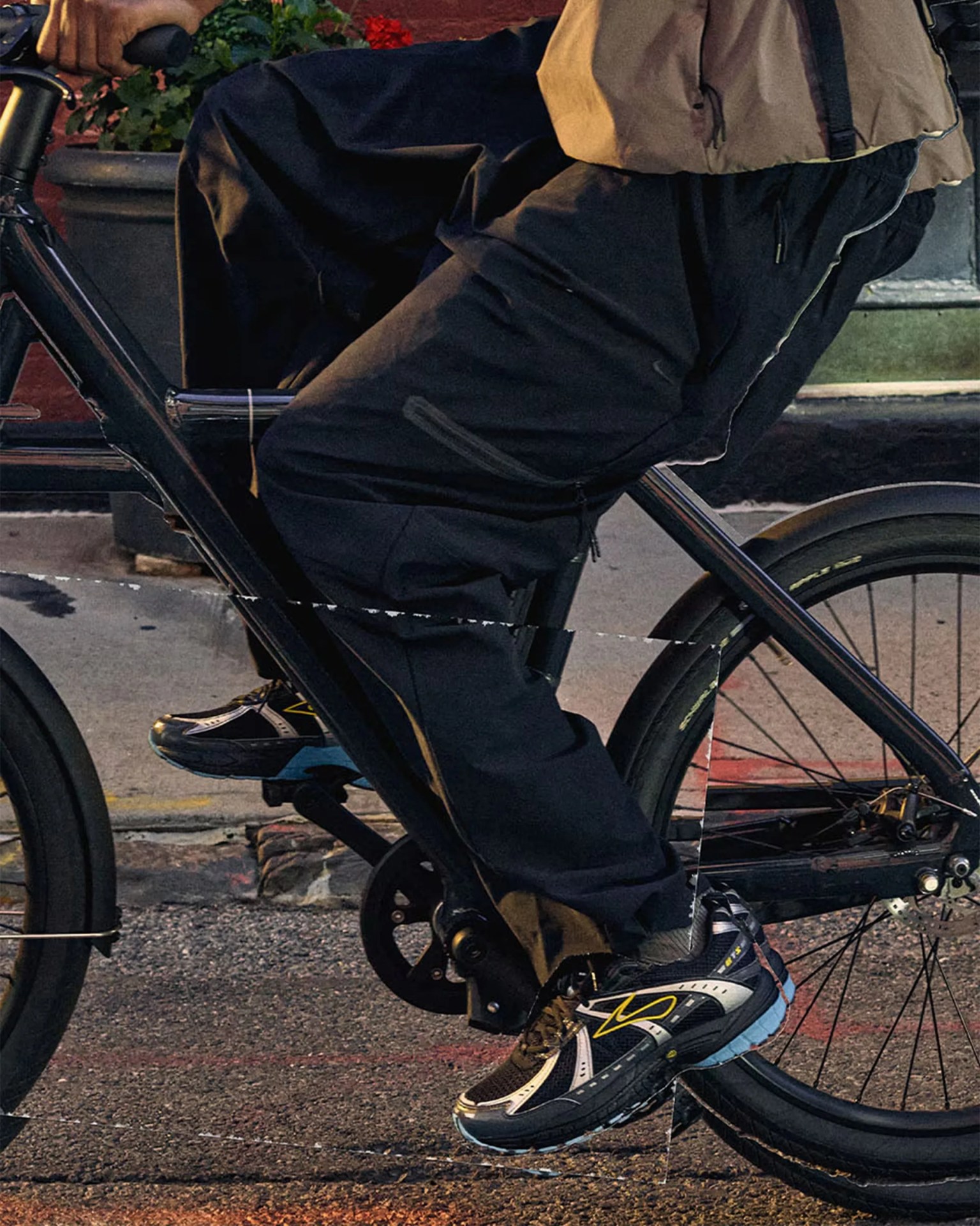Person wearing black pants and black sneakers with yellow accents riding a black bicycle on a city street.