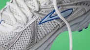 Close-up of a white and gray mesh running shoe with blue accents and white laces on a green background.