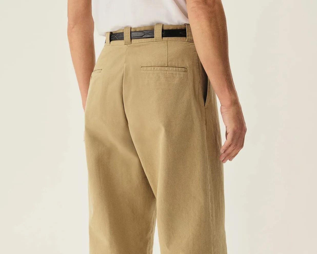 Back view of beige pants with welt back pockets and a black belt worn by a person.