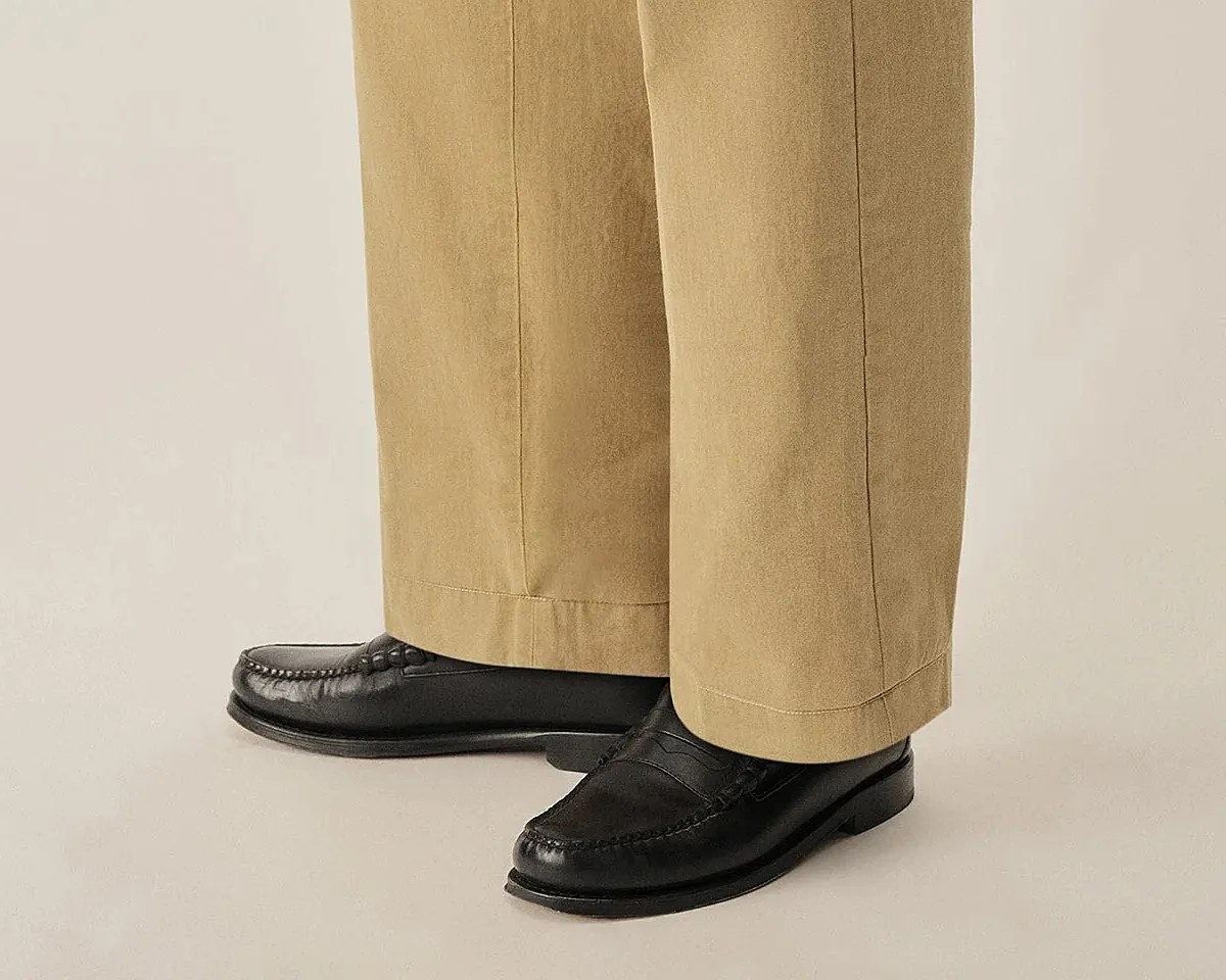 Black leather penny loafers worn with beige wide-leg trousers.