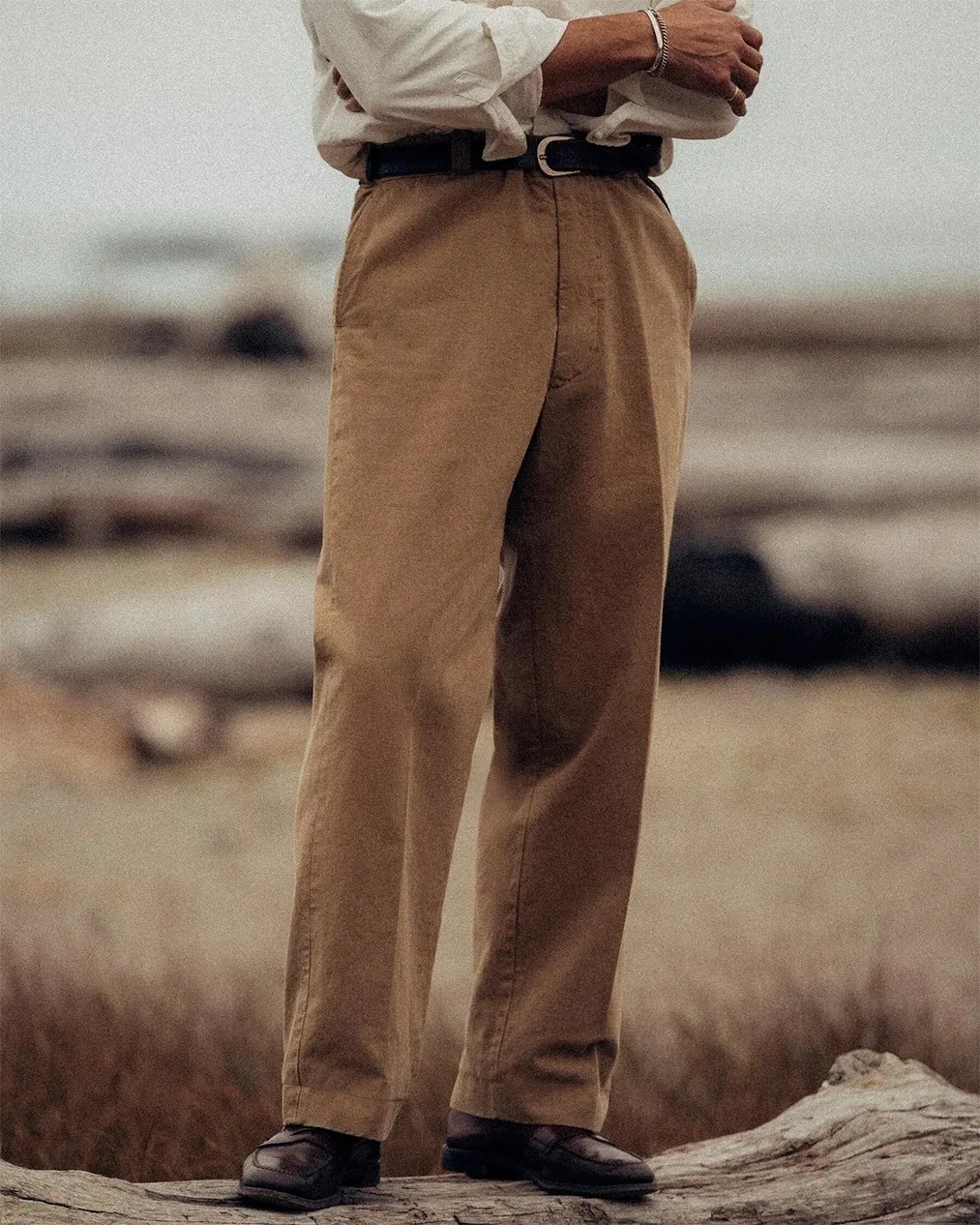 Brown straight-leg trousers paired with black belt and dark brown loafers on a natural outdoor setting.