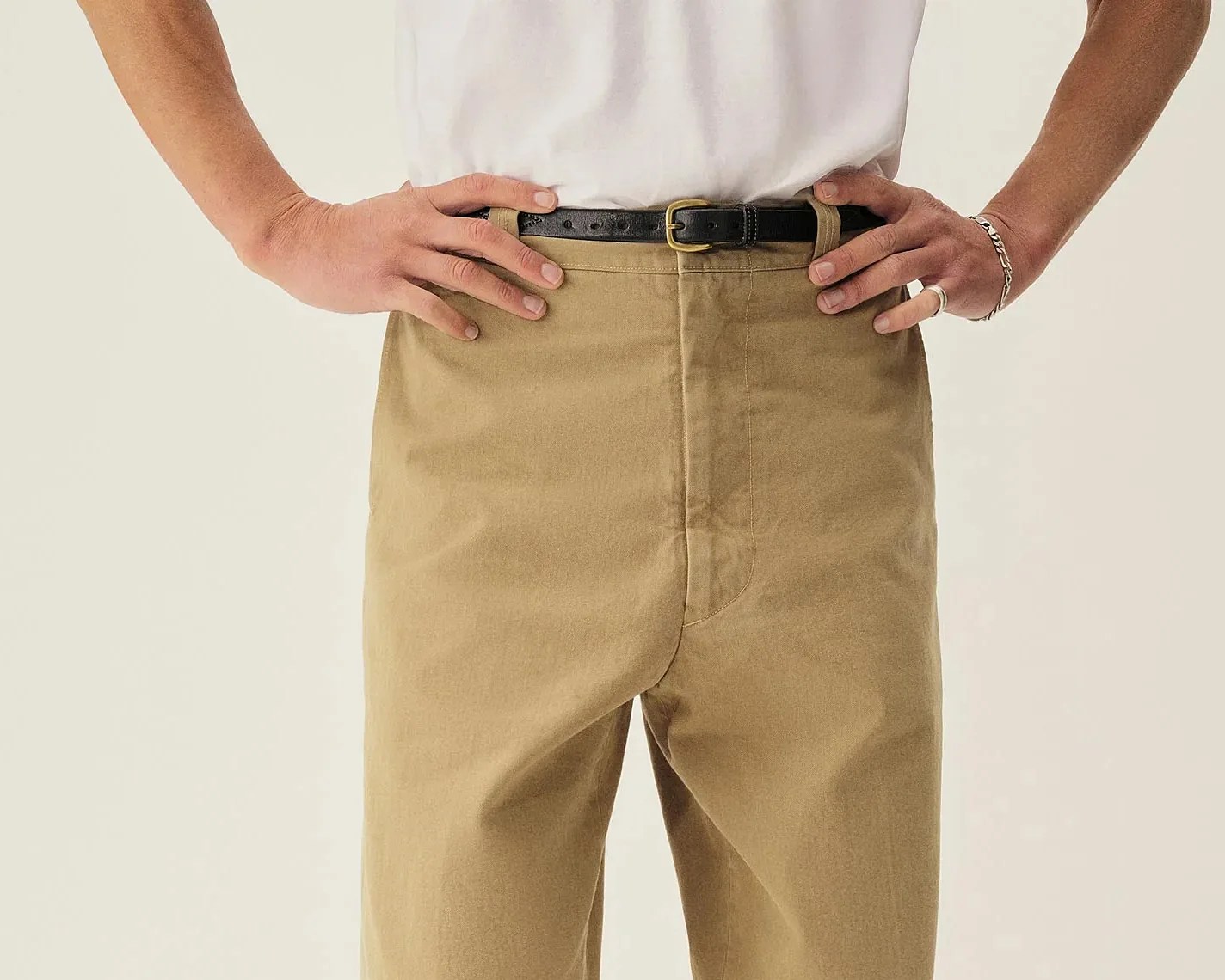 Close-up of a person wearing tan pants with a black leather belt and a white shirt tucked in.