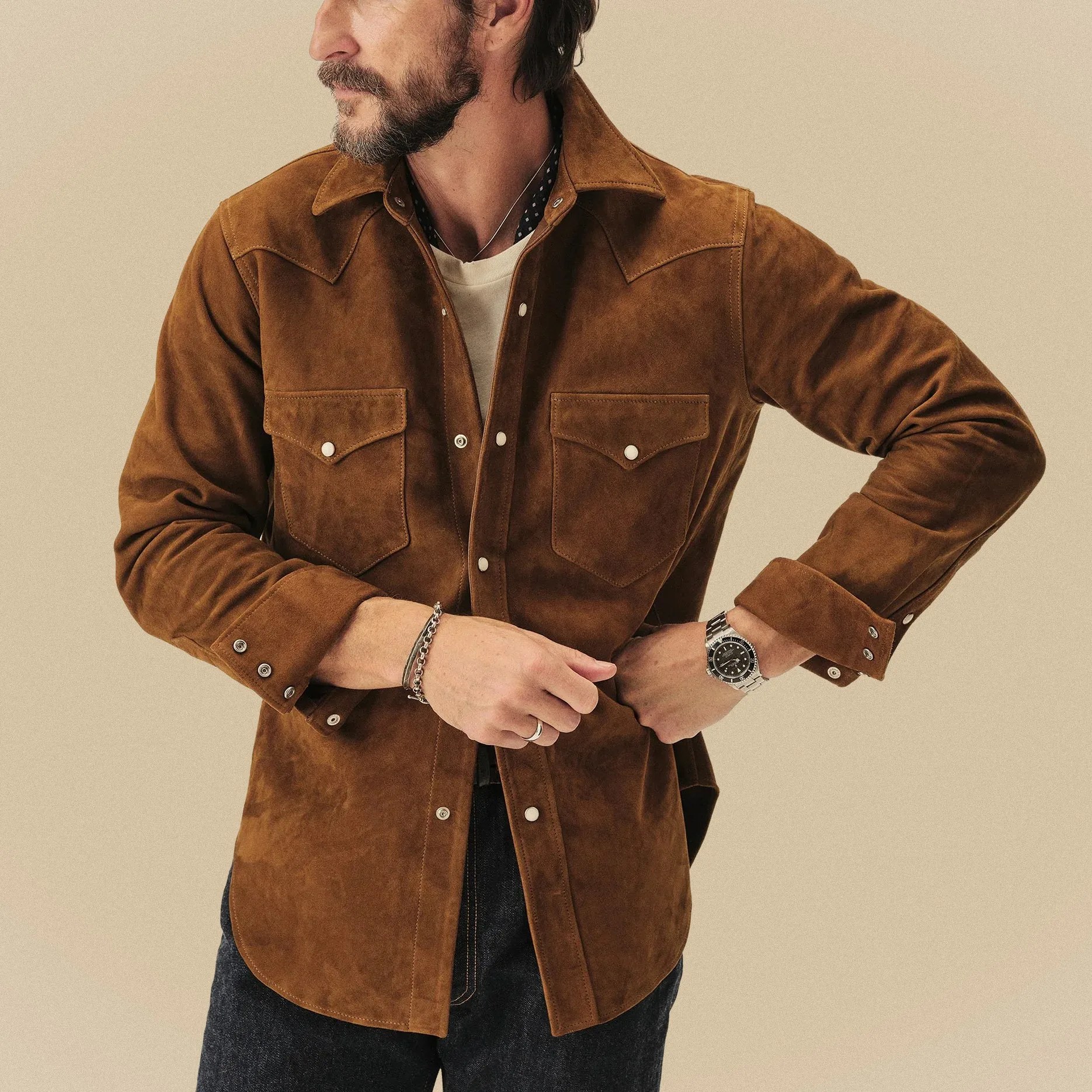 Brown suede button-up shirt with flap chest pockets worn by a person adjusting the cuff.