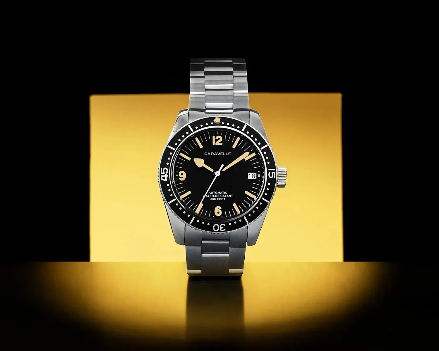 Stainless steel Caravelle wristwatch with black dial, beige markers, and date display on a reflective surface.