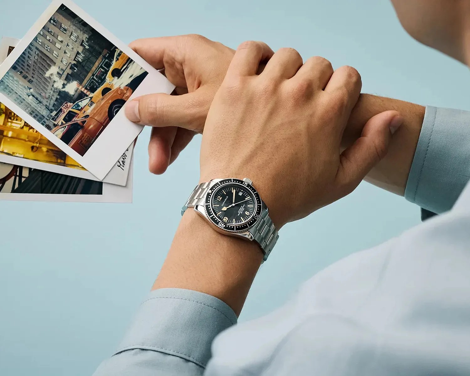 Silver metal wristwatch with black dial and rotating bezel worn on a wrist holding vintage-style photos.