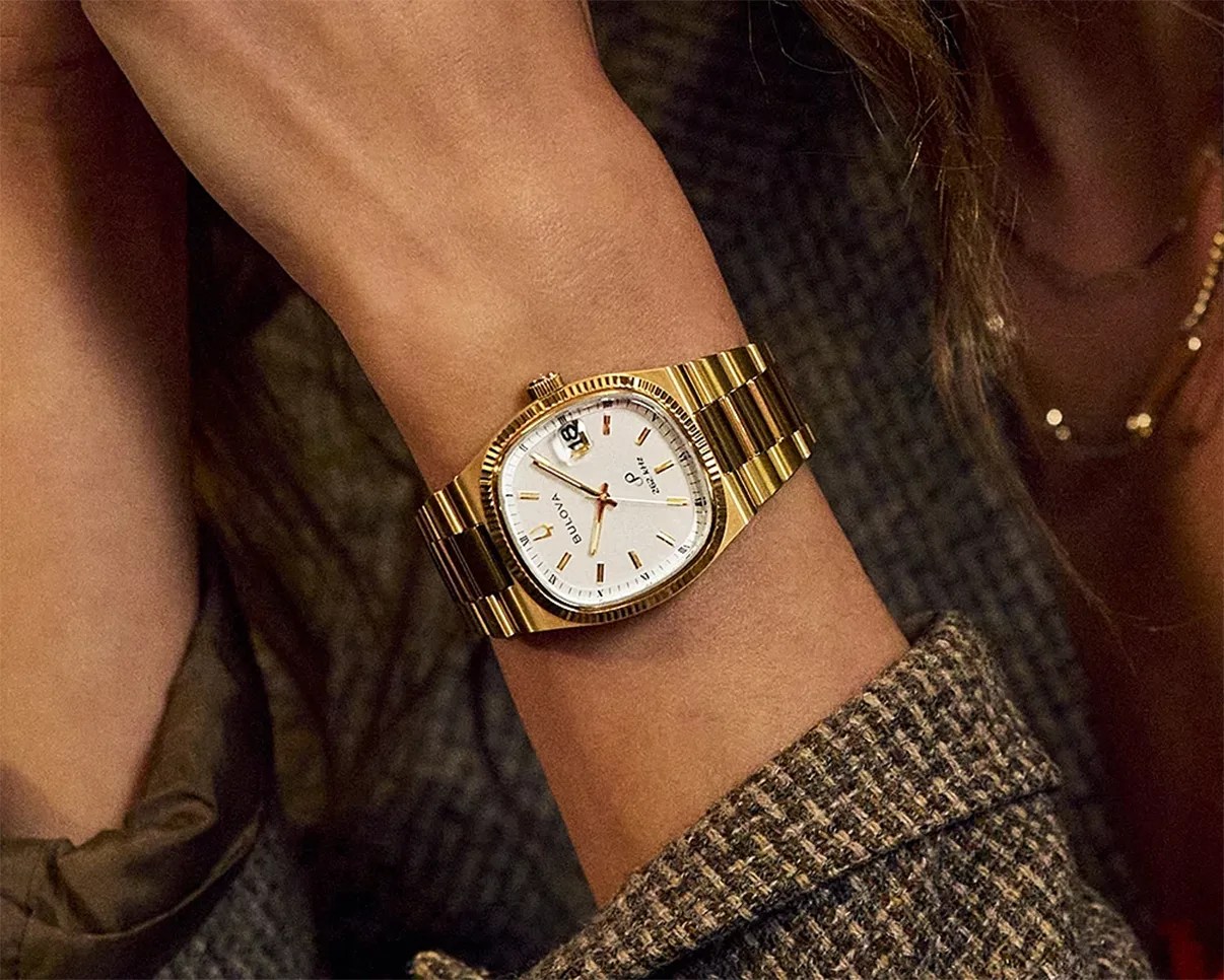 Gold-tone Bulova wristwatch with white dial and date display worn on a wrist.
