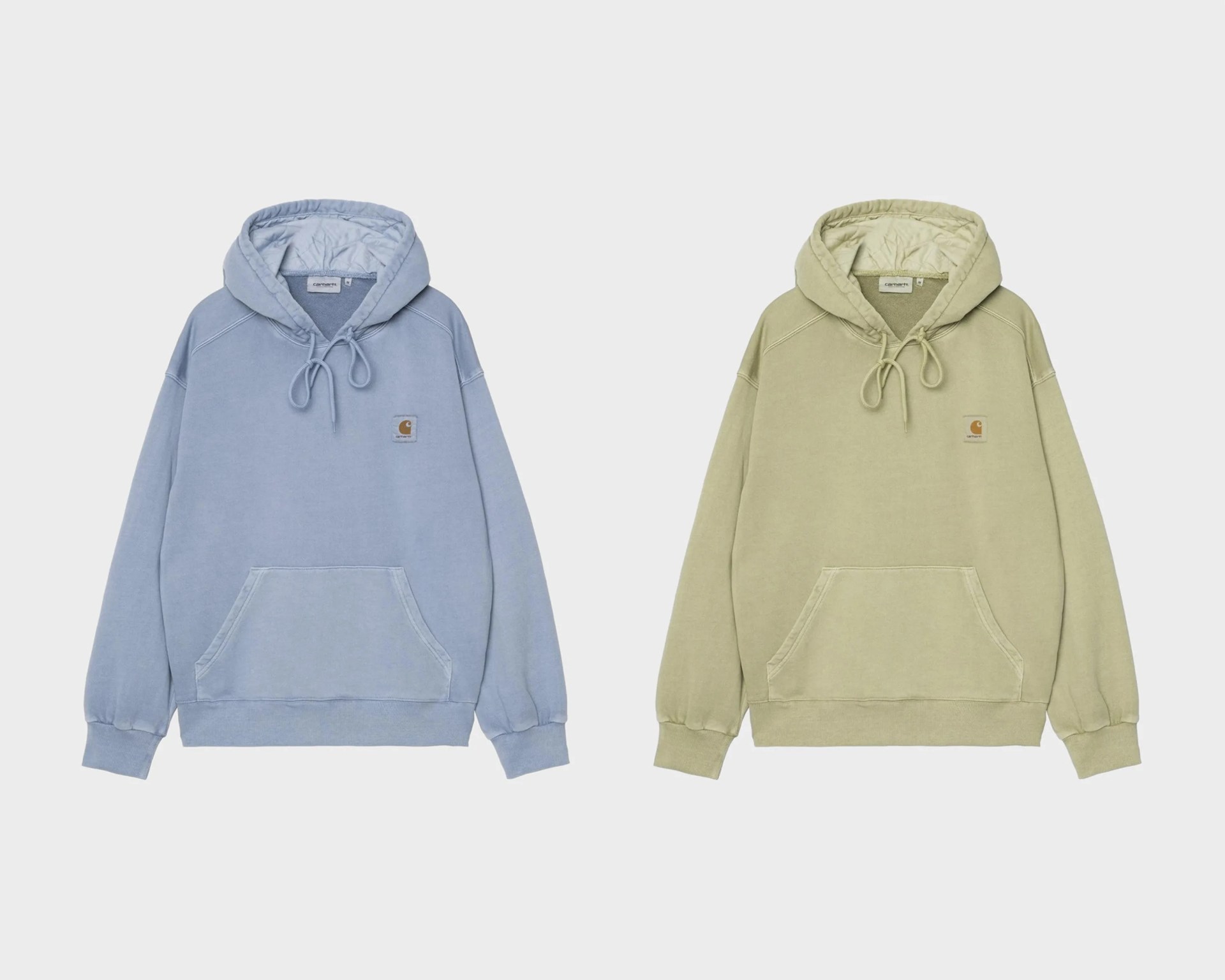 Two Carhartt hoodies side by side, one in light blue and the other in light olive green, both with front pockets and drawstring hoods.
