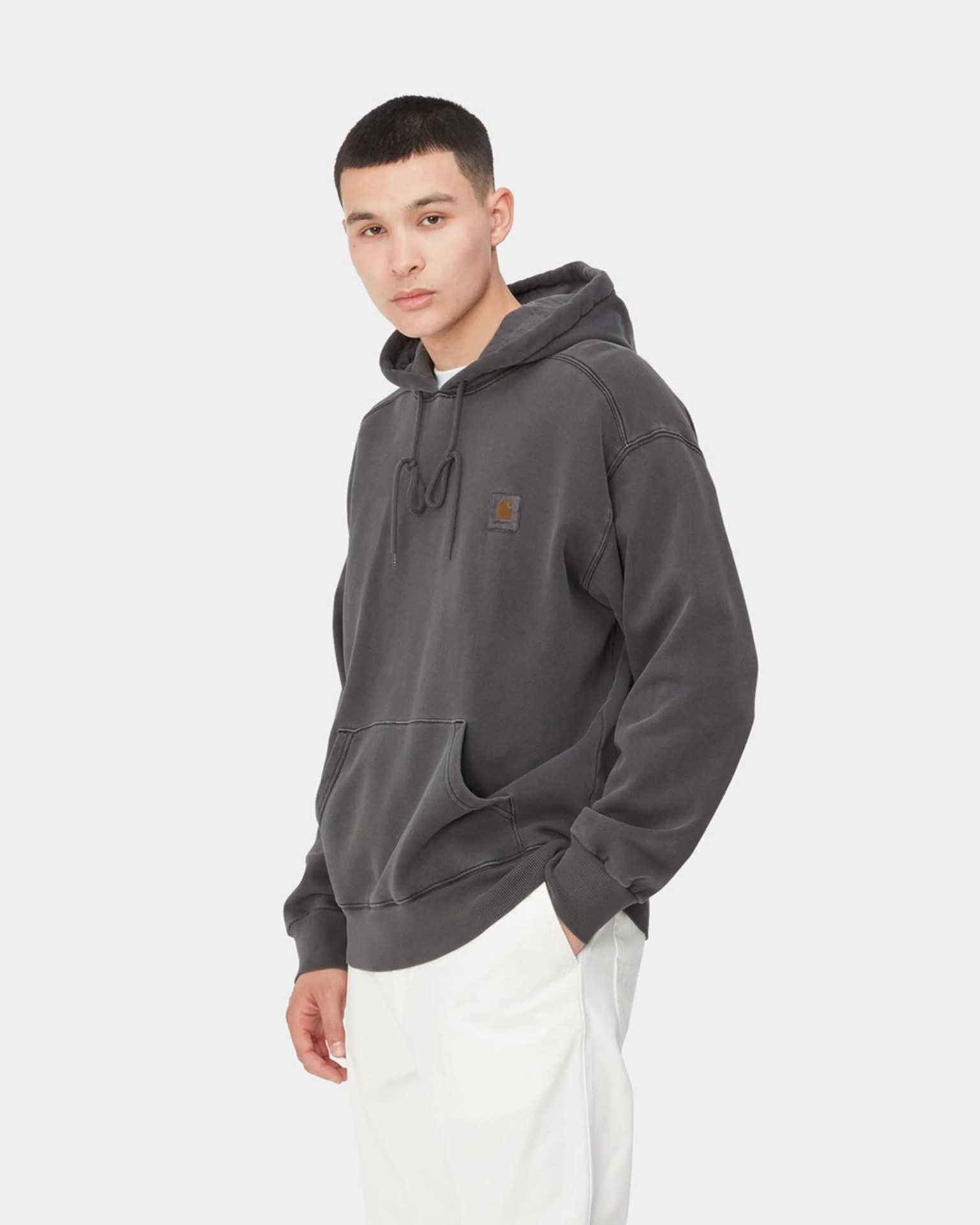 Charcoal gray Carhartt hoodie with front pocket and logo patch worn by a person with white pants.