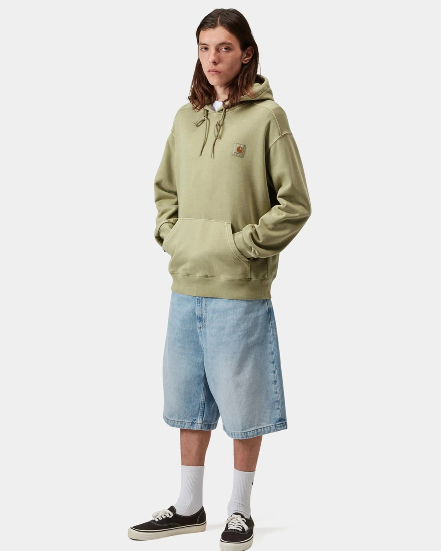 Person wearing an olive green Carhartt hoodie, light blue denim shorts, white socks, and black sneakers.