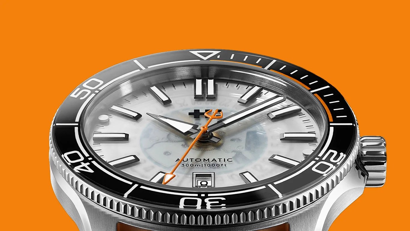 Close-up of a stainless steel automatic dive watch with black bezel, white dial, and orange second hand on an orange background.