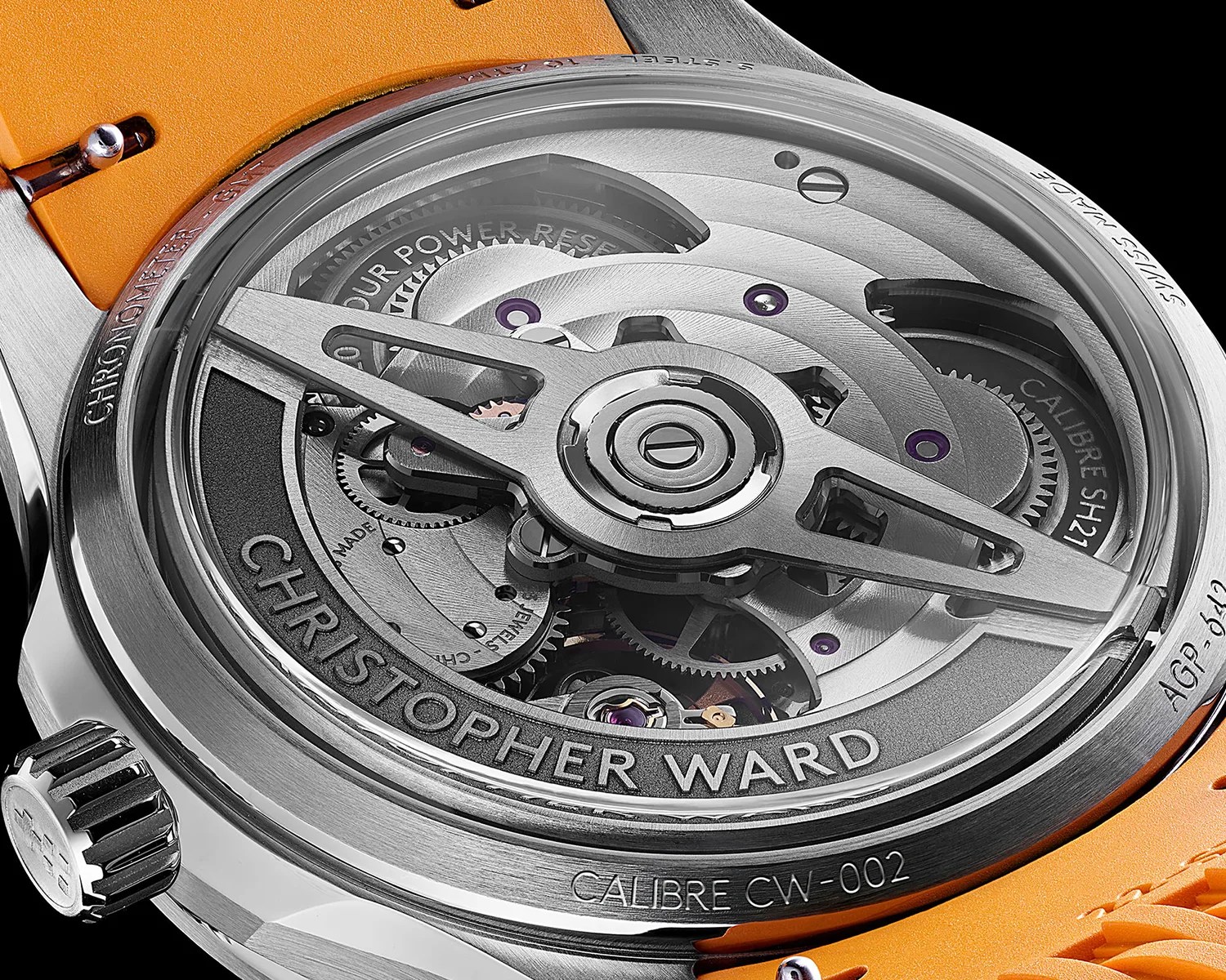 Close-up of the back of a Christopher Ward watch showing the intricate silver mechanical movement and orange strap.