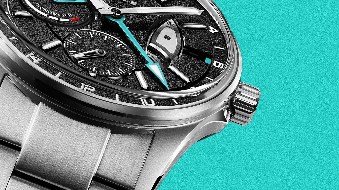 Close-up of a stainless steel wristwatch with a black textured dial and turquoise-tipped hands on a turquoise background.