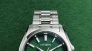 Silver titanium Citizen wristwatch with green textured dial and silver hour markers on a green background.