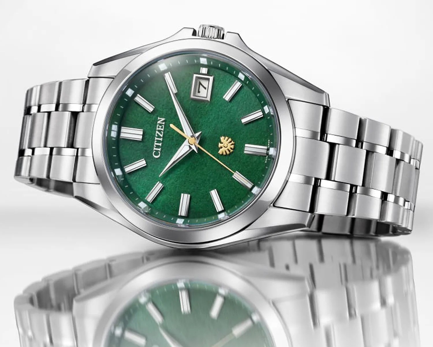 Silver titanium Citizen wristwatch with a textured green dial and gold second hand on a reflective surface.