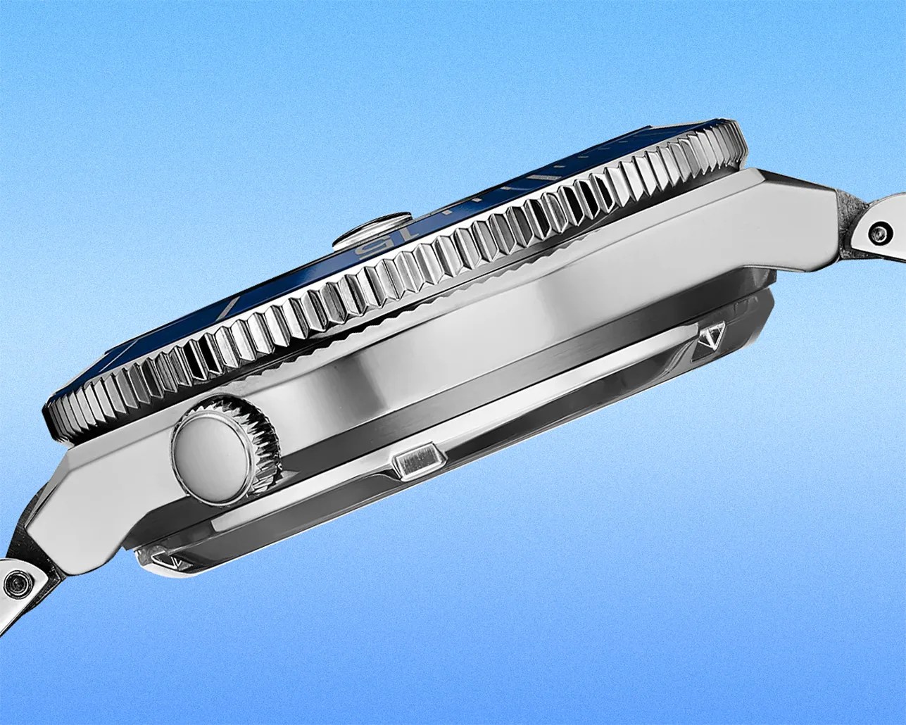 Side view of a silver stainless steel watch case with a ridged bezel and crown against a blue background.