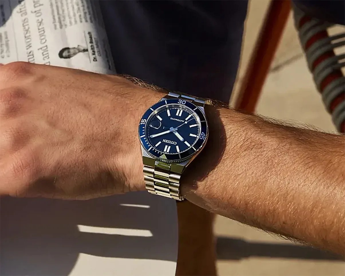 Silver metal Citizen wristwatch with blue dial and bezel worn on a wrist.