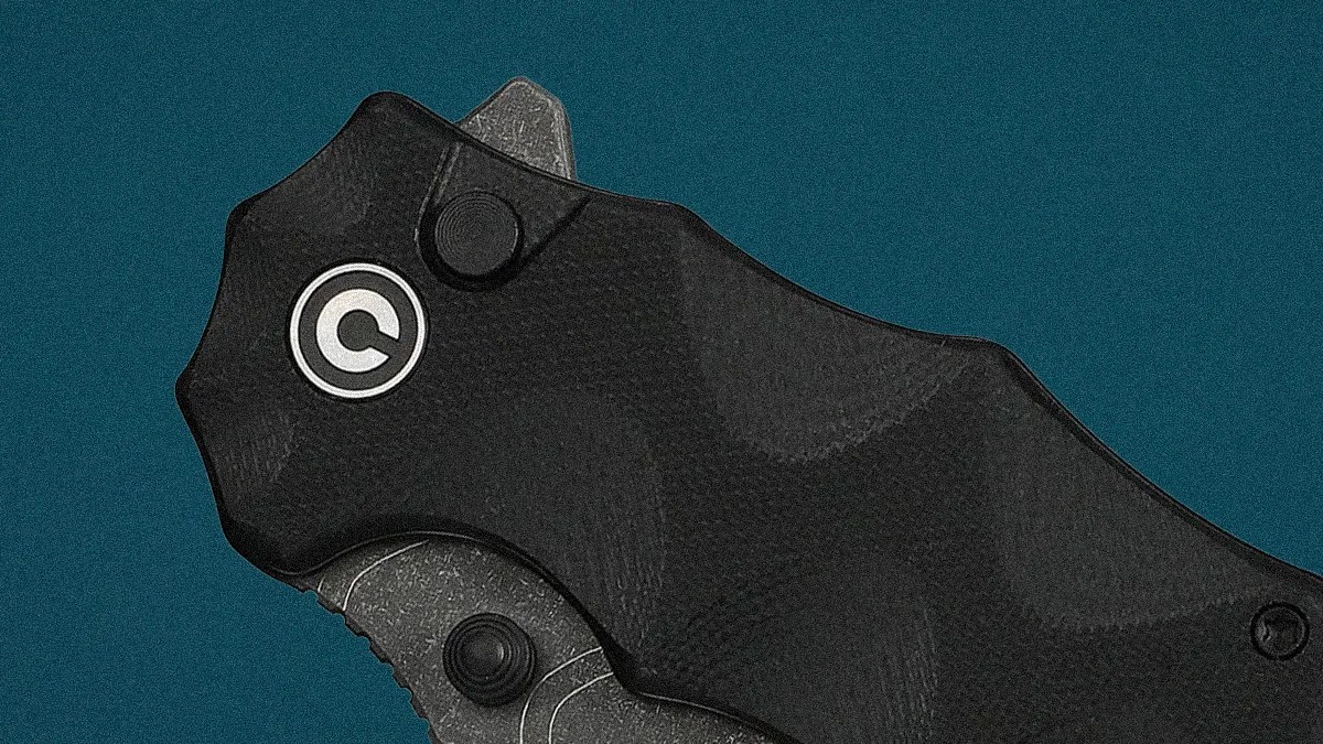 Close-up of a black folding knife handle with a circular logo on a teal background.