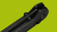 Close-up of a black folding knife hinge and textured handle against a green background.