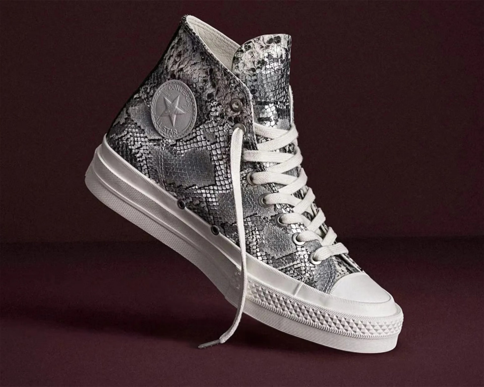 High-top Converse sneaker with black and white snakeskin pattern and white rubber sole on a dark background.
