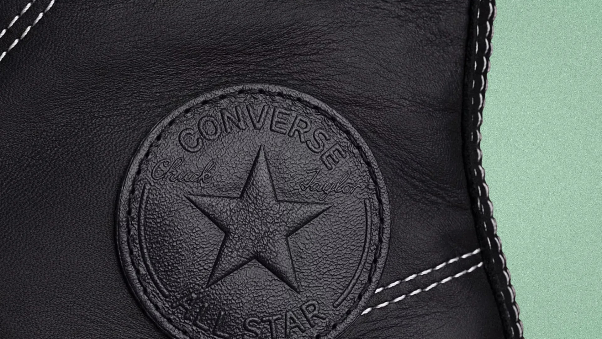Close-up of a black leather Converse Chuck Taylor All Star patch with white stitching on a shoe.