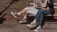 Two people sitting on a park bench wearing Converse sneakers, one in patchwork high-tops and the other in black-and-white plaid low-tops.