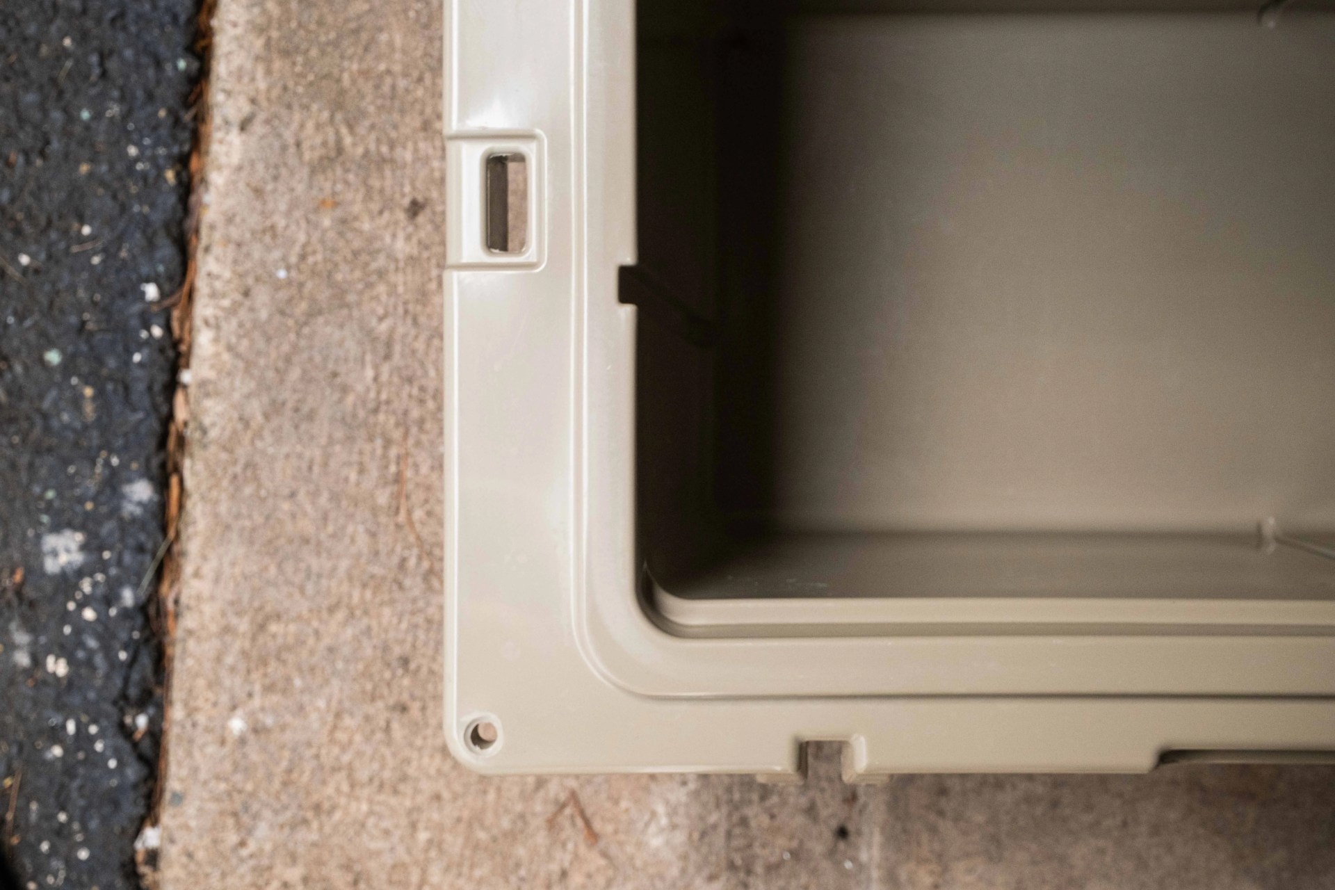 Beige plastic storage container corner on a concrete and asphalt surface.