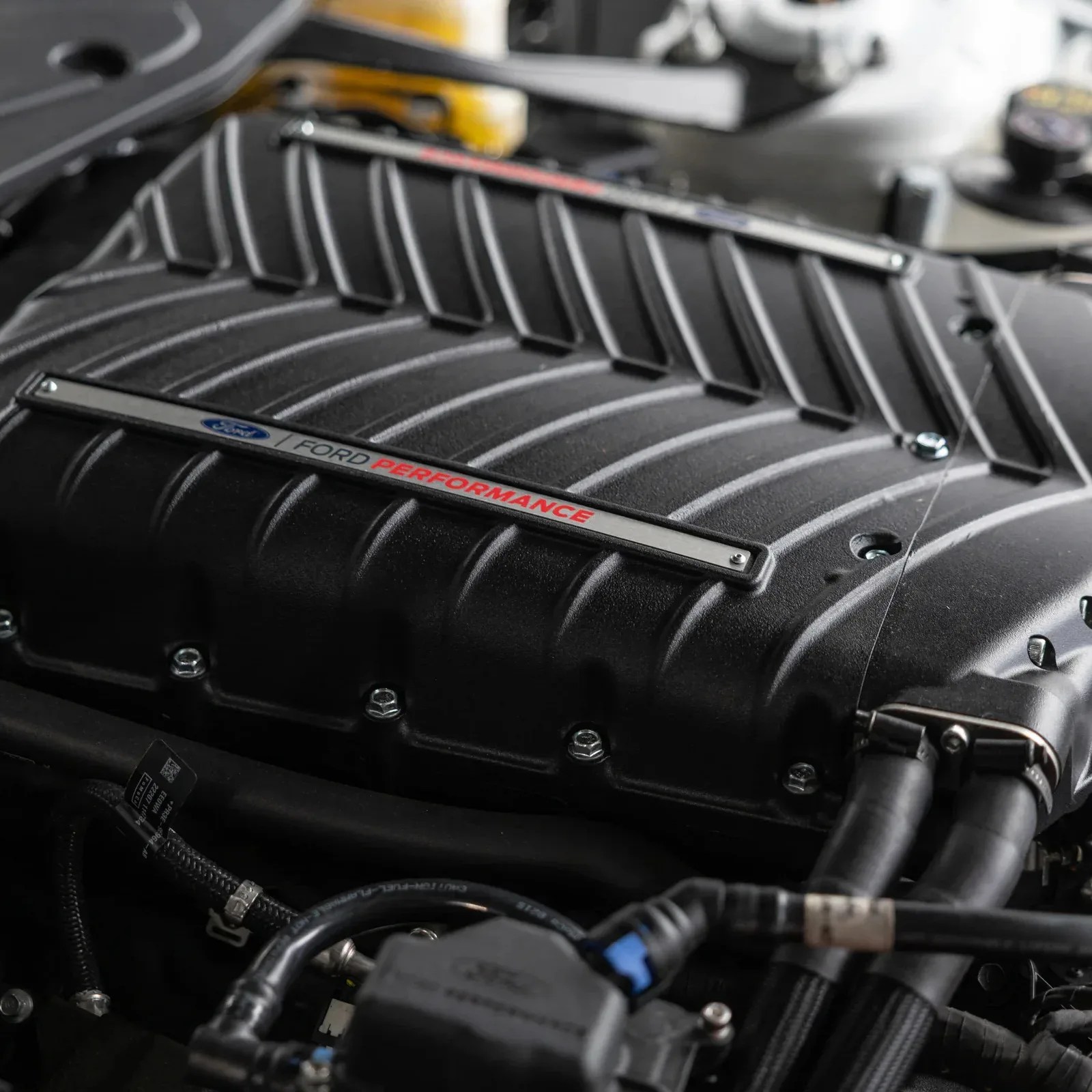 Close-up of a black Ford Performance engine cover with visible bolts and hoses.