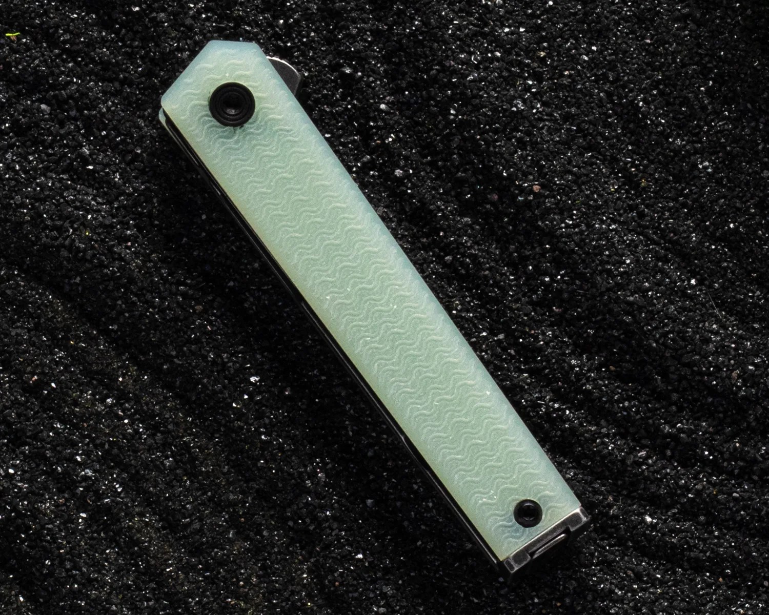 Closed folding knife with a textured light green handle on black gravel.